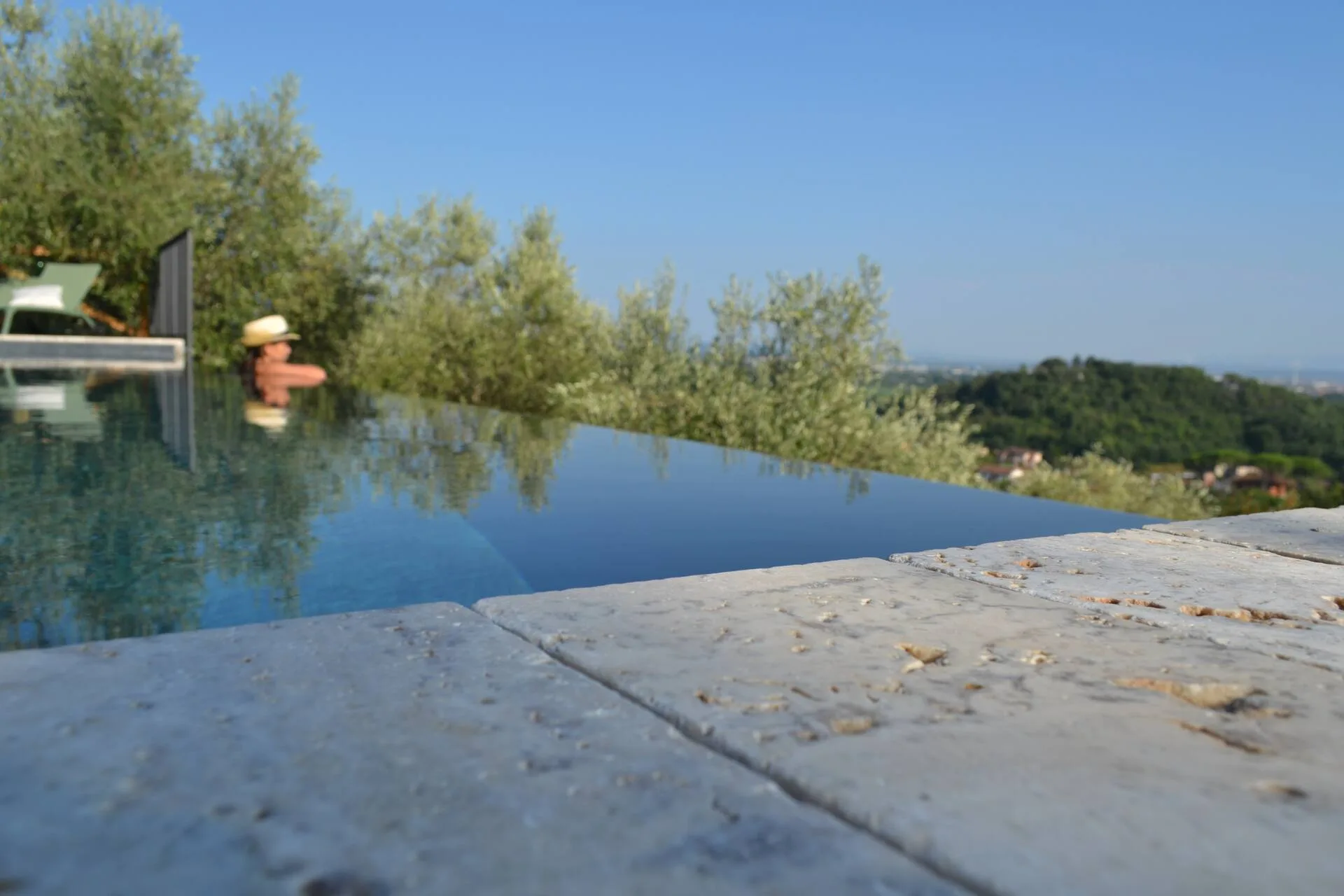 Close view along the pool's stone coping toward the olive grove